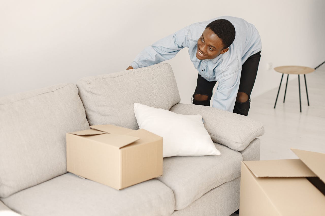 about-01 Young man smiling while arranging cardboard boxes in a modern living room.