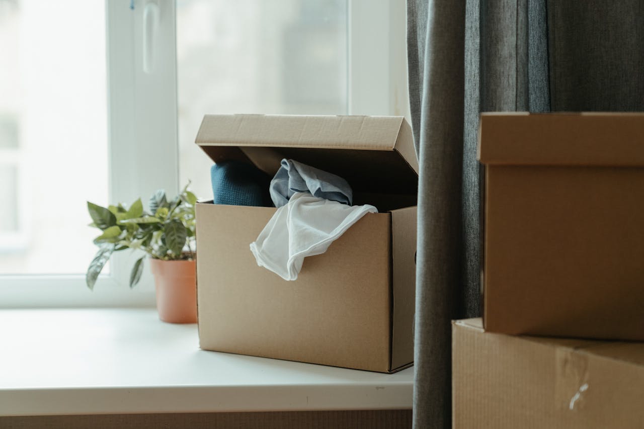 home-services-02 Open cardboard box with clothes by window, symbolizing moving or relocation.