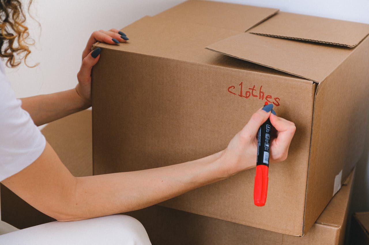 home-services-03 Close-up of a woman labeling a cardboard box with a red marker indoors.